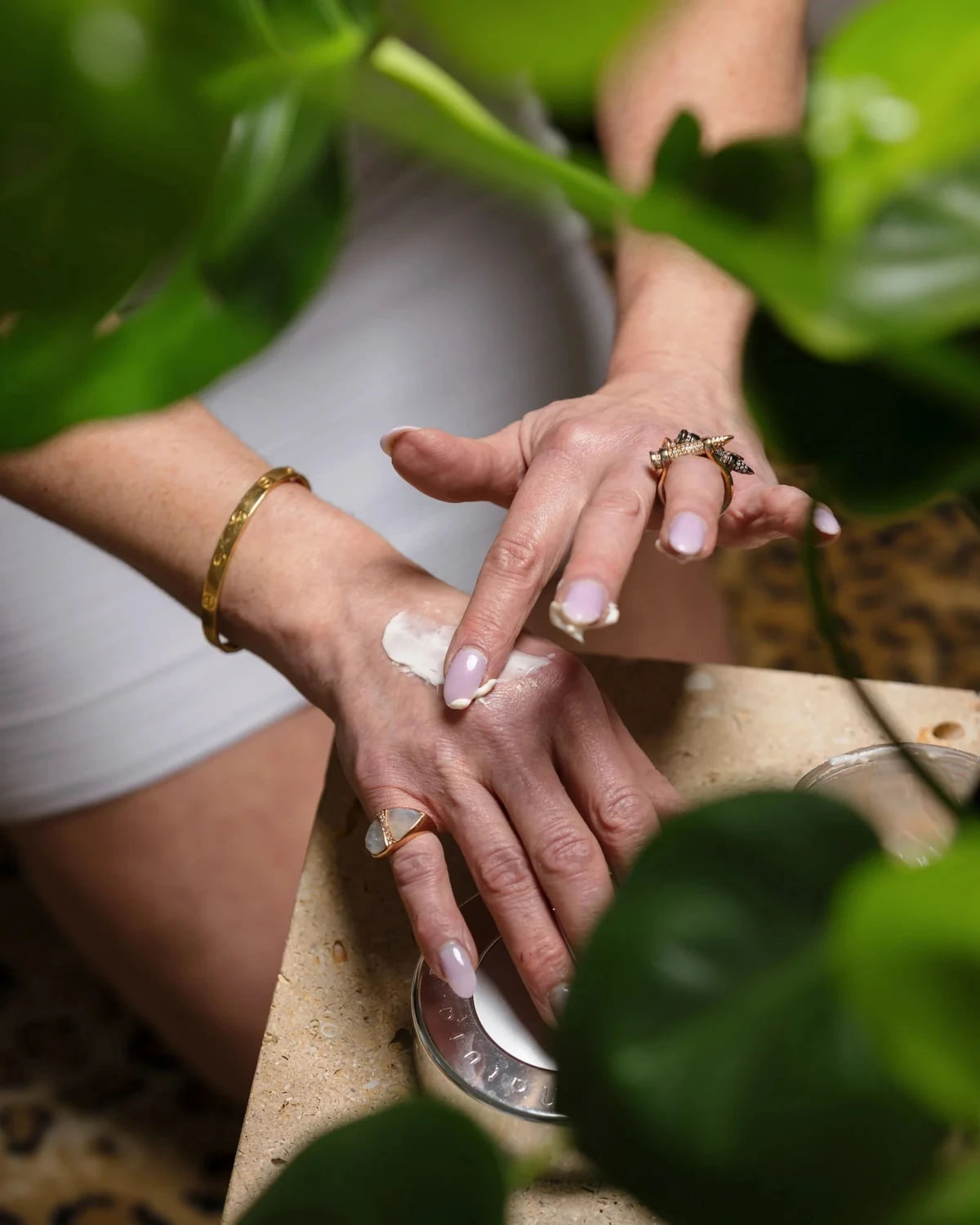 Hands holding an open jar of cream among green leaves